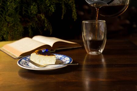Cup of coffee and slice of cheesescake with open book on wooden table.の写真素材