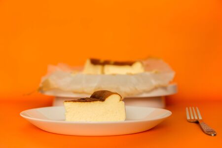 Slice of Basque Burnt Cheesecake on a plate with fork in orange background.