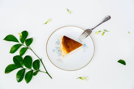 Slice of basque burnt cheesecake on plate with dessert fork on white background.