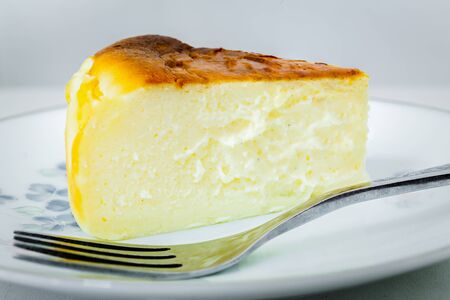 Macro slice of basque burnt cheesecake and fork on plate in white background.の写真素材
