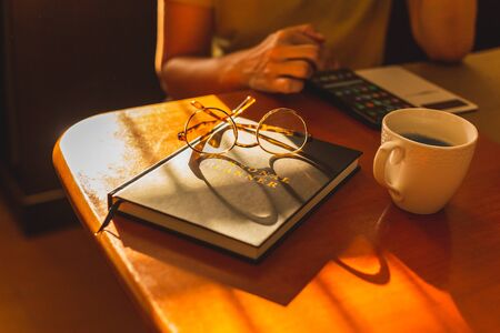 Woman hands checking smart phone with personal organizer diary with eyeglasses and coffee mug on table at homeの写真素材