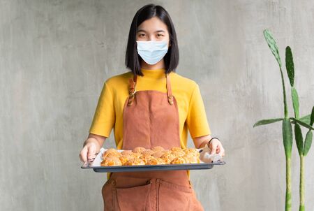 Woman in medical mask holding baking tray with choux cream SME concept.