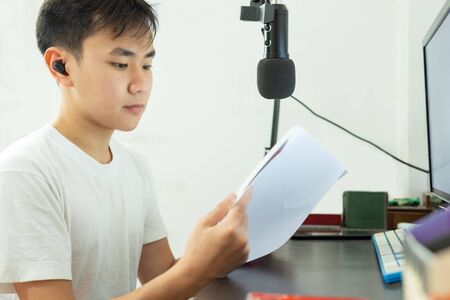 Asian boy study on a book with microphone and pc on the table study at home.の写真素材