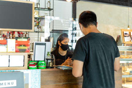 New nomarl customer at counter with staff behind plastic partition in cafe covid-19 protection.の写真素材