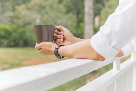 Man relaxjng hand holding coffee mug while standing on balcony.