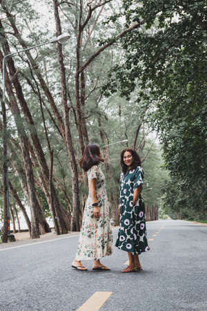 Woman wearing beautiful long dress standing on the road under green treesの写真素材