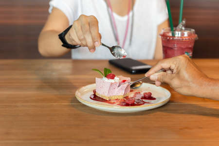 Hands eating currant mousse cake with spoon in cafe.の写真素材
