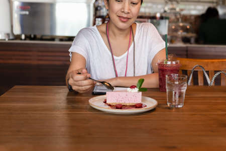 Happy woman eating currant mousse cake with spoon in cafe.の写真素材
