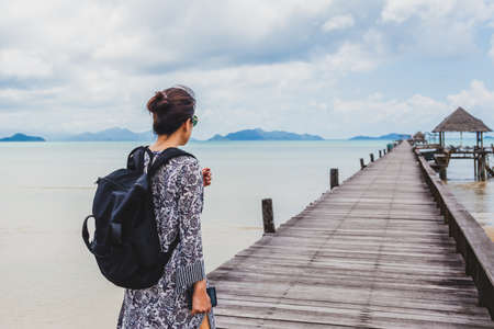 Woman in summer dress walking on wooden bridge with peaceful seascape.の写真素材