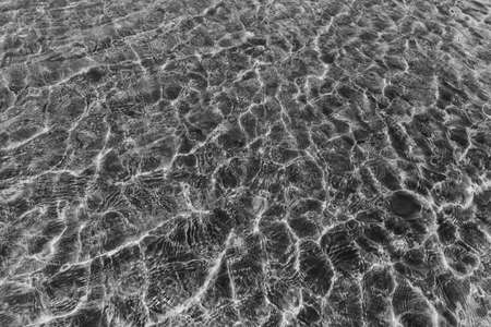 Top view surface of clear sea water reflections on shallow sandy beach.