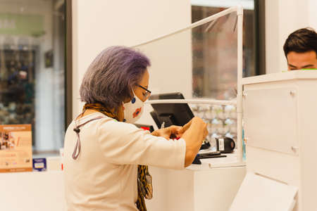 Senior customer wearing protective mask paying money at cashier counter.