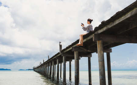Woman taking photo on cell phone while sitting on the wood bridge.の写真素材