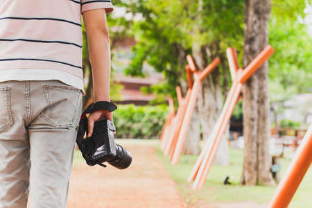 Back view of tourist man holding digital camera in his hand walking in the park outdoor.の写真素材
