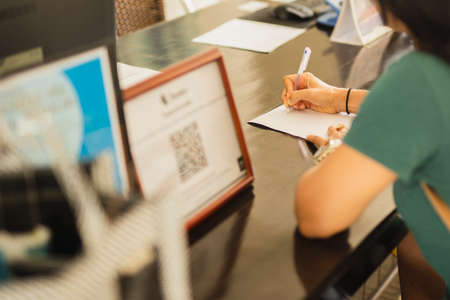Businesswoman hand signing hotel agreement contract at reception desk.の写真素材