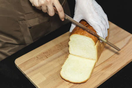 Hand cutting homemade Japanese Hokkaido bread on wooden board.の写真素材