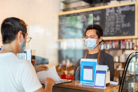 New normal waiter service customer at cafe counter with partition protection.の写真素材