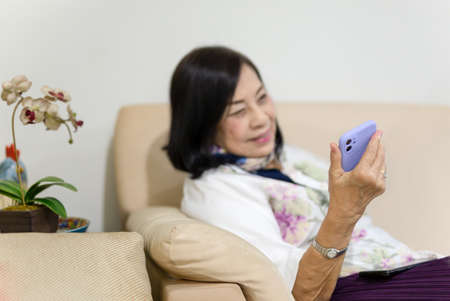 Selected focus happy senior woman sitting on couch using phone for video call.