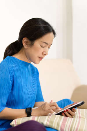 Woman sit on couch at home using cell phone texting chatting with friend.の写真素材