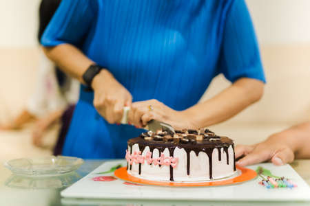 Woman is hand cutting birthday cake together with family.