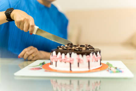 Woman is hand cutting birthday cake in blur backgroung.