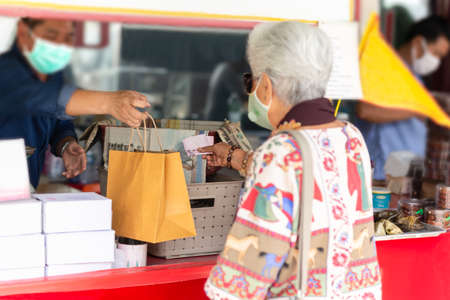 Man with protective mask giving to eldery woman food products in paper bag.