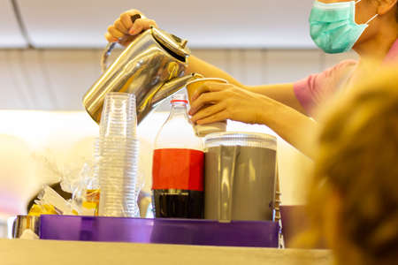Flight attendant in facial mask protection from covid-19 serves passengers a drink.の写真素材