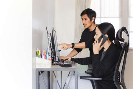 Asian couple working on computer together at homeの写真素材