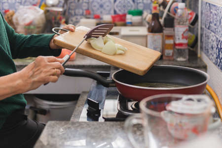 Senior woman putting onions in frying pan.の写真素材
