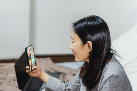 Happy woman sit on bed at home video calling friend on smartphone.の写真素材
