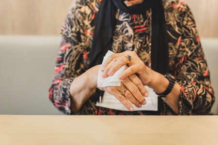 Woman in medical mask cleaning her hands with a wet wipes in restaurant.の写真素材