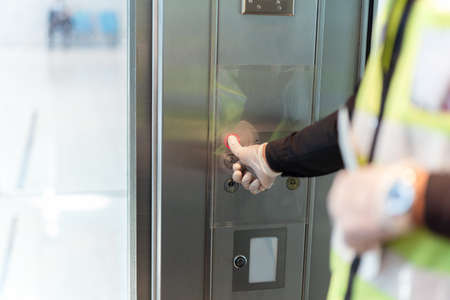 Security man hand in protective glove against virus presses lift button.