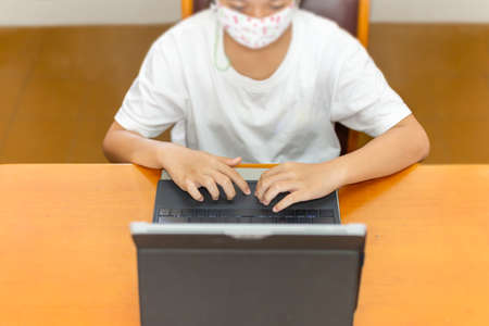 Young student with protective mask hands typing on laptop.の写真素材