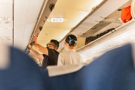 Flight atttendant attendant helping passenger to put luggage cabin compartment.の写真素材