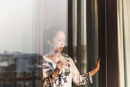 Shot through window woman relaxing holding botttle of water.