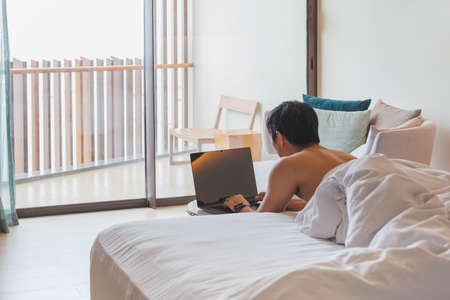 Man working on laptop lying in bed on vacation.の写真素材