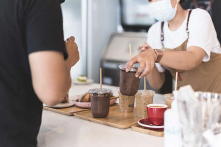Waitress wearing protection face mask serving iced chocolate drink to customer in cafe.の写真素材