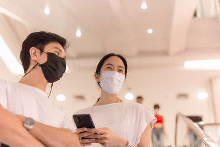 Couple in protective mask standing on escalator in the shopping mall.