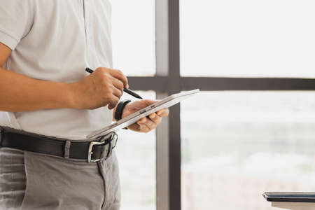 Businessman standing next to the window in his office holding digital tablet.