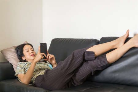 Woman lying on a couch using smartphone.の写真素材