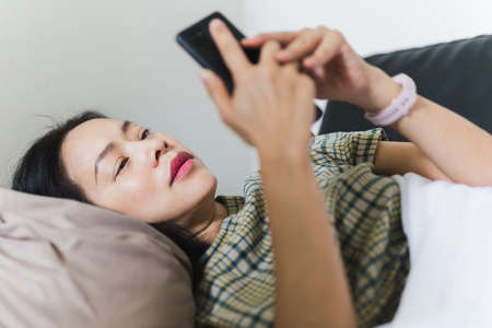 Portrait of woman lying down on a couc holding cell phone.の写真素材