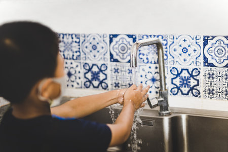Asian little boy hand washing with tap water in kitchen sink during covid-19.の写真素材