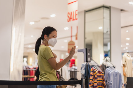Woman in protective mask hand measuring thermometer temperature while entering shopping mall.の写真素材