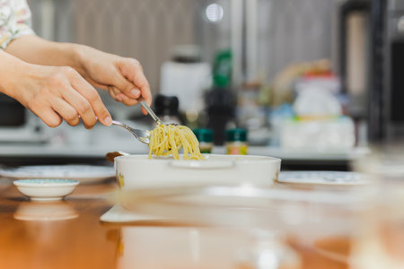 Woman eating creamy spaghetti carbonara with folk and spoon at dinner table.の写真素材