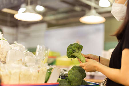 Women in protective mask pick up broccoli in vegetable store.の写真素材