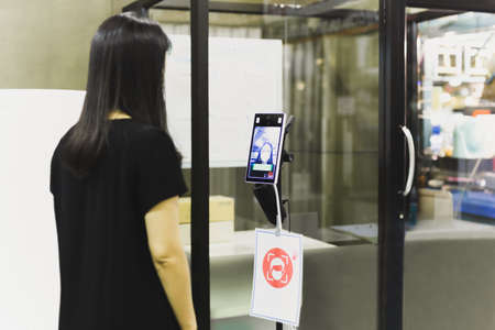 Woman in medical mask scanning body temperature using thermal scanner.