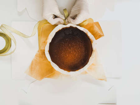 Female baker hand with glove packing basque burnt cheesecake cake with ribbon.の写真素材