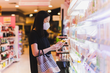 Asian woman in protective mask holding bottle of shampoo in supermarket.の写真素材