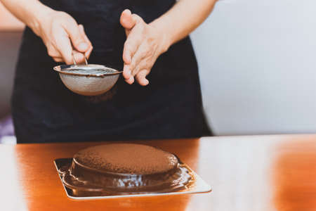 Woman wearing apron powdering chocolate cake with cocoa powder.の写真素材