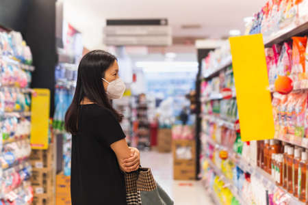 Asian woman with protective mask choosing food in supermarket during coronavirus pandemic.の写真素材