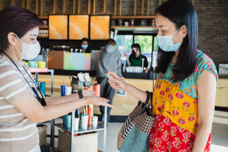 Two female in face mask friends spraying their hands with antiseptic spray in cafe.の写真素材